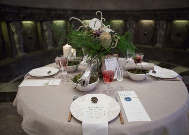 Hochzeitswahn - Ein elegant gedeckter Esstisch mit einem üppigen Tafelaufsatz, feinem Porzellan und Kristallstielgläsern, begleitet von personalisierten Menüs und Gedecken – alles bereit für ein anspruchsvolles kulinarisches Erlebnis.