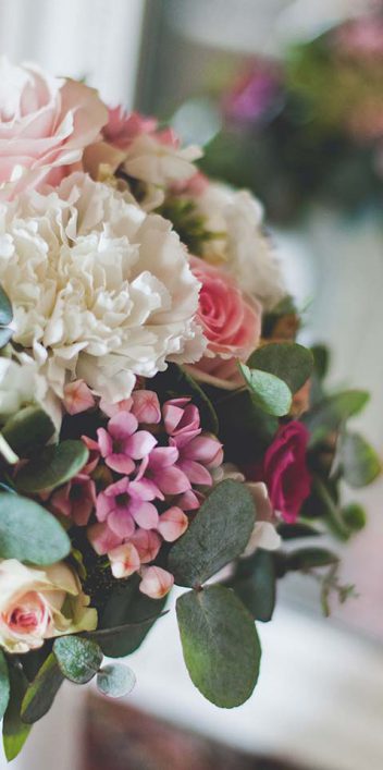 Hochzeitswahn - Ein wunderschöner Hochzeitsstrauß mit rosa Rosen, weißen Hortensien und grünen Eukalyptusblättern, elegant arrangiert und vor einem sanft verschwommenen Innenhintergrund platziert.