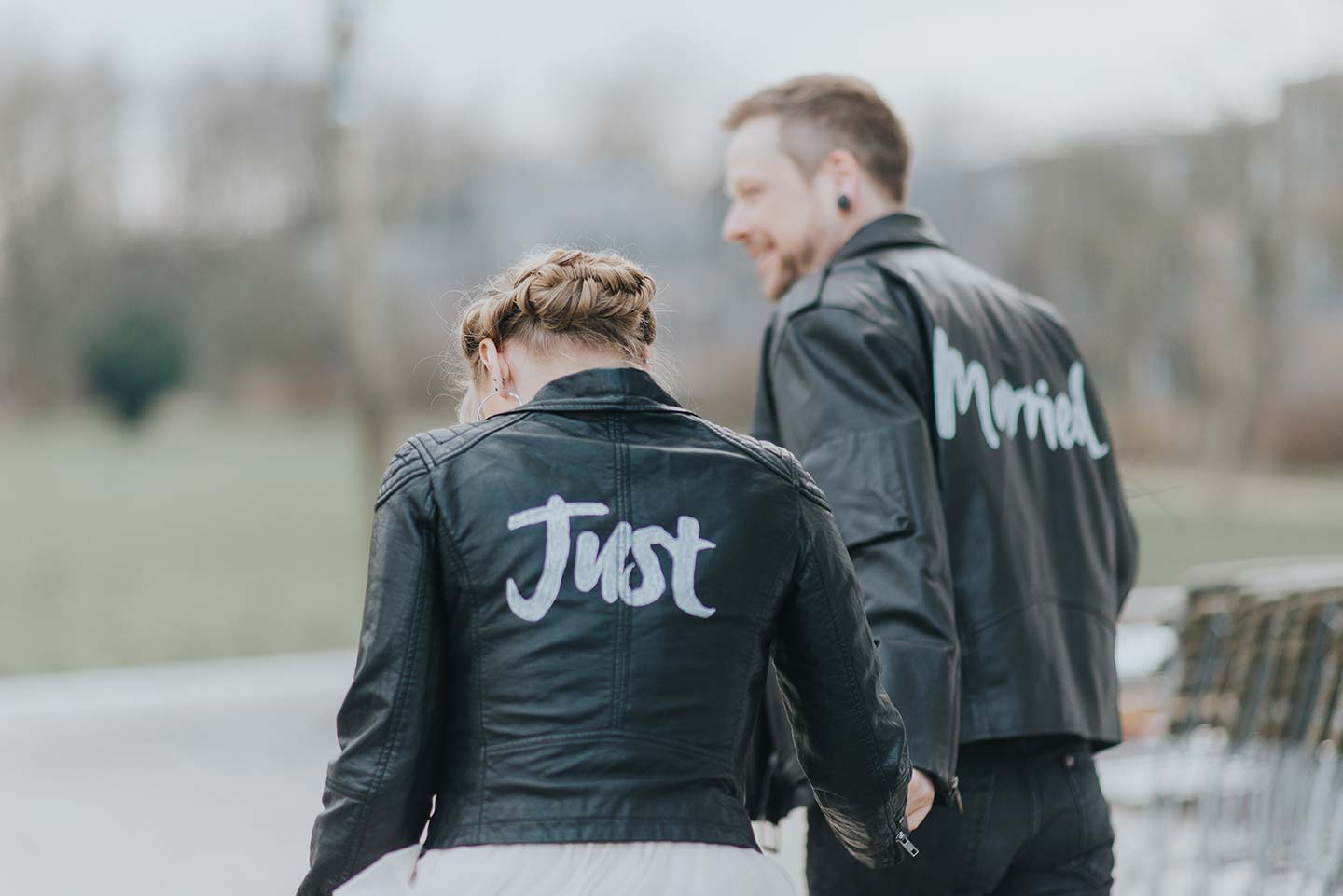 Hochzeitswahn - Ein Paar in passenden schwarzen Lederjacken geht zusammen. Auf ihren Rücken sind die Worte „gerecht“ und „verheiratet“ zu sehen, was den Beginn ihrer Reise als Ehepaar symbolisiert.