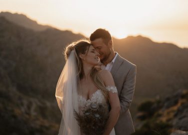 Hochzeitswahn - Eine Braut und ein Bräutigam verbringen einen zärtlichen Moment inmitten eines goldenen Sonnenuntergangs, umgeben von ruhigen Bergen, und fangen die romantische Essenz ihres Hochzeitstages ein.