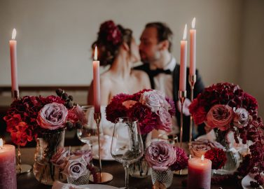 Hochzeitswahn - Eine Braut und ein Bräutigam sitzen an einem Tisch mit Kerzen und Blumen.