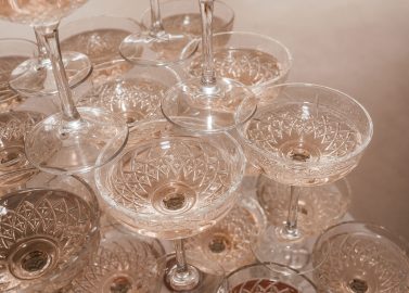 Hochzeitswahn - Eine Nahaufnahme mehrerer übereinander gestapelter leerer Champagnergläser. Die Gläser sind klar und haben ein dekoratives Muster in den Schalen, das das Licht reflektiert und einen funkelnden Effekt erzeugt. Die Oberfläche unter den Gläsern ist beige. Hochzeit in der Kulturfabrik Coburg.