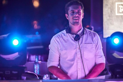 Hochzeitswahn - Eine Person mit weißem Hemd und Kopfhörern steht hinter DJ-Equipment und wird von blauen Bühnenlichtern angestrahlt. Die Szene lässt vermuten, dass Fabian Baroud in einem Club oder bei einer Veranstaltung auftritt. Hochzeit in der Kulturfabrik Coburg.