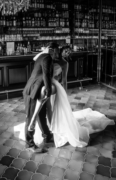 Hochzeitswahn - Ein Mann im Anzug küsst eine Frau im trägerlosen Brautkleid, während sie ein Bein anhebt. Die beiden stehen zusammen auf einem gemusterten Fliesenboden – dieser romantische Moment wurde von Francesco Calarota Photography wunderschön eingefangen. Zuckerbergschloss-Kappelrodeck-Hochzeit