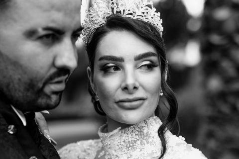 Hochzeitswahn - Eine Nahaufnahme eines Schwarzweißfotos von Francesco Calarota zeigt eine Braut in einem detailreichen Spitzenkleid und einer juwelenbesetzten Krone, die wegschaut, während der Bräutigam mit ernstem Gesichtsausdruck nach vorne blickt – zeitlose Momente durch FC Art Photography. Zuckerbergschloss-Kappelrodeck-Hochzeit
