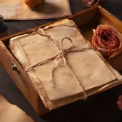 Hochzeitswahn - In einer Holzkiste liegt ein Bündel alter, vergilbter Briefe, die mit Bindfäden zusammengebunden sind, begleitet von getrockneten Rosen und Vintage-Umschlägen – eine perfekte Inspiration für kreative Hochzeitseinladungen oder jeden, der Hochzeitseinladungen selbst basteln möchte.